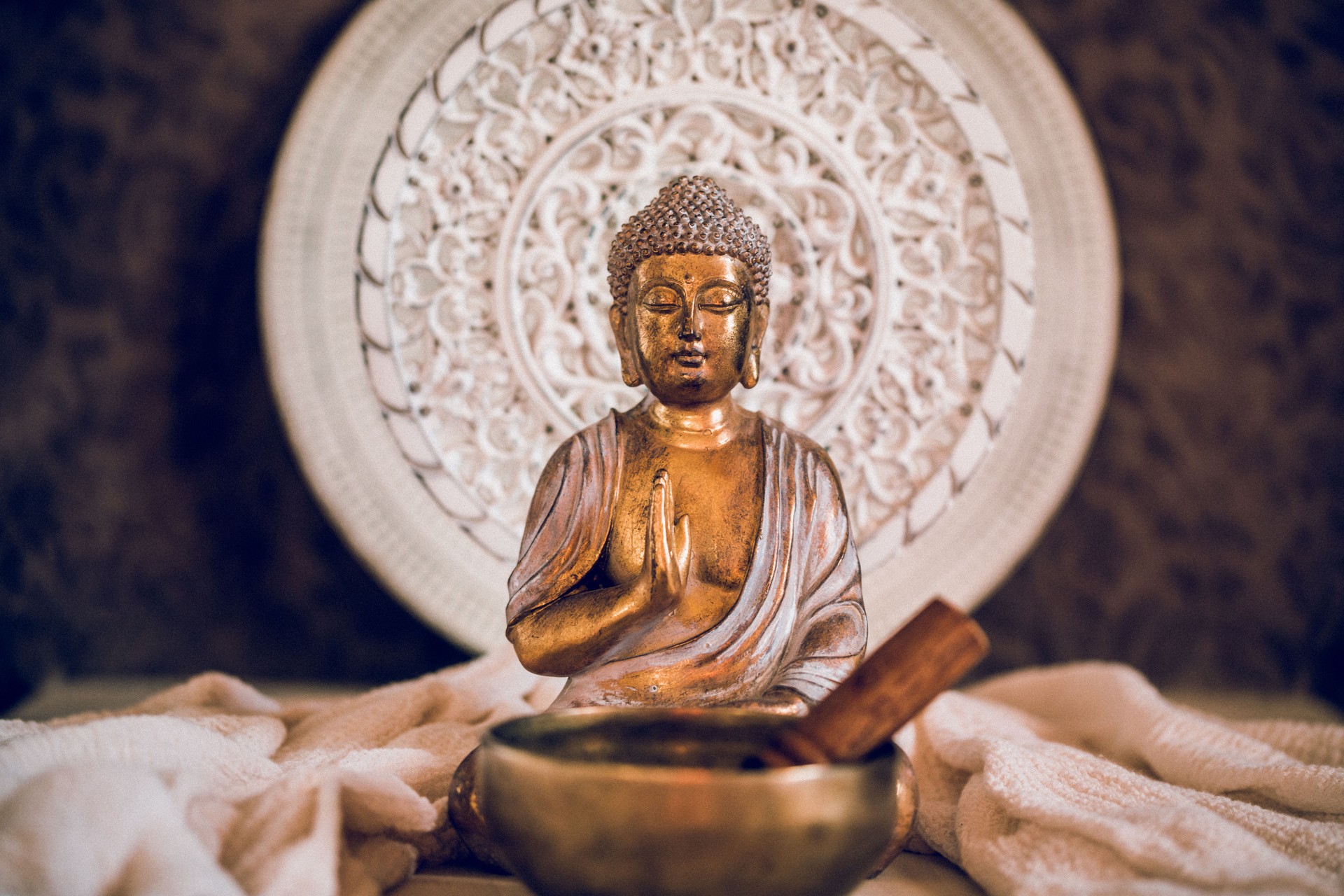 Golden Buddha with a Tibetan singing bowl in front of a white wooden mandala